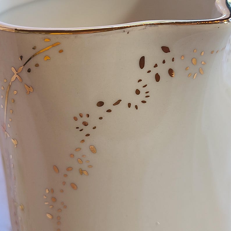 May include: A white ceramic pitcher with a gold rim and delicate gold floral designs.