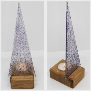May include: A glass candle holder shaped like a triangle with a speckled, frosted finish. The holder sits on a wooden base and has a small tea light candle inside.