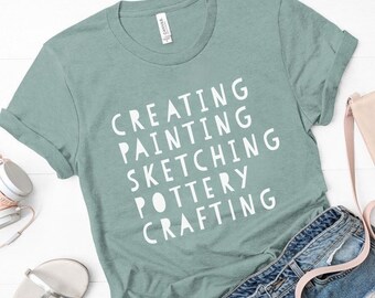 May include: A light blue t-shirt with the words "Creating", "Painting", "Sketching", "Pottery", and "Crafting" printed in white.