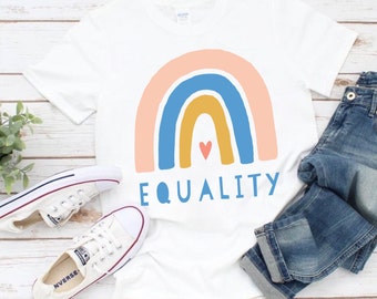 May include: White t-shirt with a rainbow design and the word "EQUALITY" printed on the front. The rainbow is made up of pink, blue, yellow, and orange stripes. There is a small pink heart in the center of the rainbow.