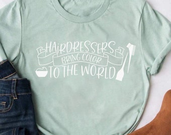 May include: A light green t-shirt with a white graphic that says "Hairdressers bring color to the world". The graphic also includes a bowl of hair dye and a comb.