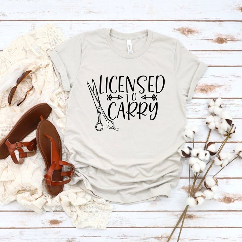 May include: A light grey t-shirt with the text "Licensed to Carry" and a pair of scissors.