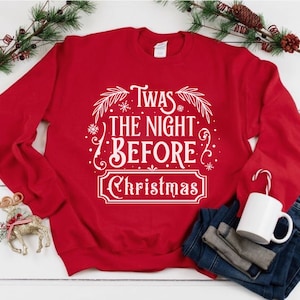 May include: Red Christmas sweatshirt with white text that reads "Twas the night before Christmas" with a decorative border of snowflakes and leaves.