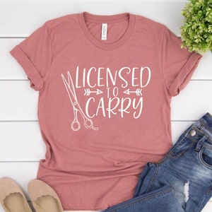 May include: A pink t-shirt with the text "Licensed to Carry" and a pair of scissors graphic.