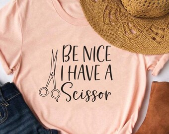 May include: A pink t-shirt with the text "Be Nice I Have A Scissor" and a pair of scissors graphic.
