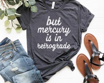 Puede incluir: Una camiseta gris oscuro con el texto "but mercury is in retrograde" impreso en blanco.