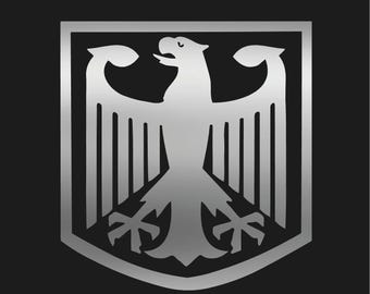 May include: A silver-colored emblem of a stylized eagle with outstretched wings, set within a shield-shaped border. The eagle is a prominent design element, with detailed feathers and a strong, forward-facing pose. The background is solid black.