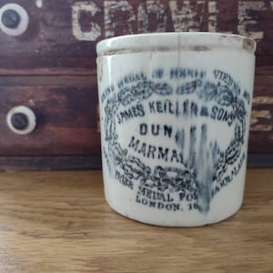 May include: A white ceramic jar with blue lettering that reads "Grand Medal of Merit Vienna 1873 James Keiller & Sons Dunmarmarmalade Prize Medal for London 1862"