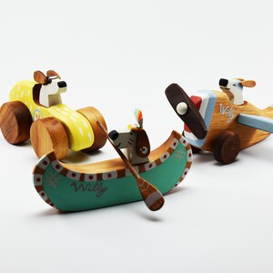 May include: Three wooden toy vehicles featuring a dog character. A yellow car, a blue and red airplane, and a green canoe with a dog paddling.