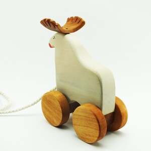 May include: A white wooden pull toy shaped like a moose with brown wooden antlers and wheels. The toy has a string attached to it.
