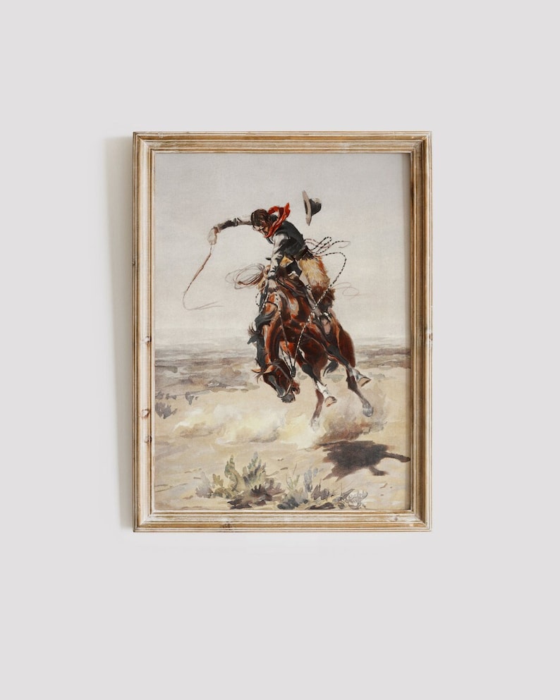 May include: A framed watercolor painting depicting a cowboy riding a bucking horse. The cowboy is wearing a red bandana and a hat, and he is holding a rope in his right hand. The horse is brown and white, and it is kicking its legs in the air. The background is a dusty, brown landscape.