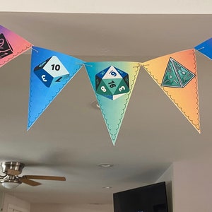 May include: A colorful banner with pennants featuring dice illustrations. Each pennant displays a different die with numbers and a unique color gradient, including pink, blue, green, and orange. The banner is strung across a room.