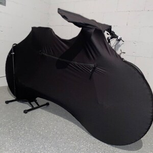 May include: Black bicycle cover with a zippered pocket. The cover is designed to fit over a bicycle and protect it from dust and dirt.