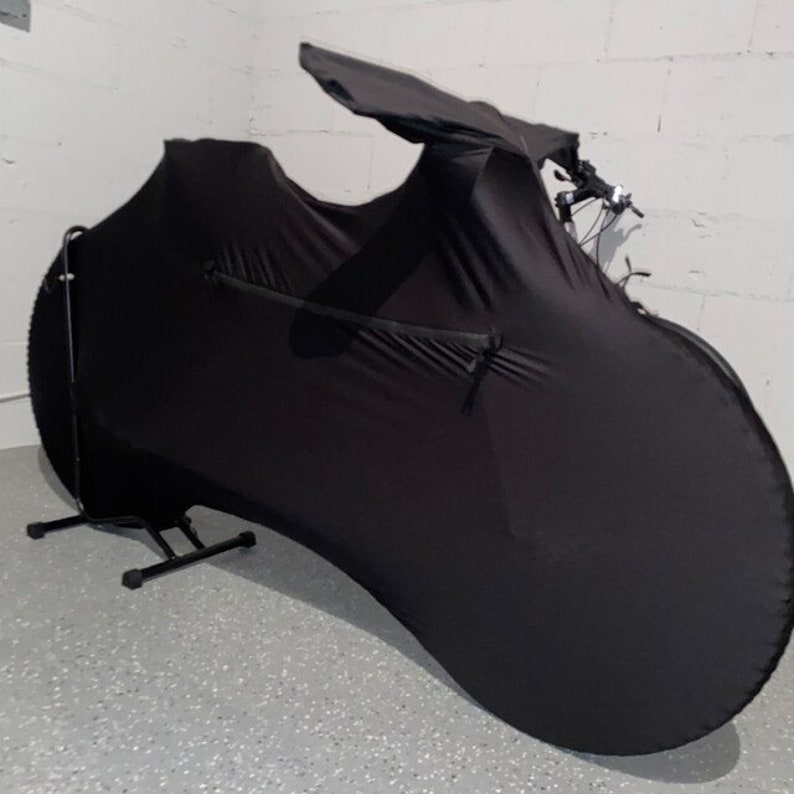 May include: Black bicycle cover with a zippered pocket. The cover is designed to fit over a bicycle and protect it from dust and dirt.