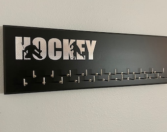 Può includere: Porta-puck da hockey nero con scritta argentata "HOCKEY" e silhouette di giocatori di hockey argentate. Il porta-puck ha 20 ganci per appendere i puck.
