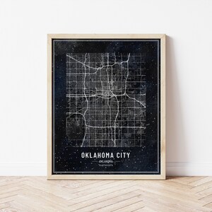 May include: A framed print of a black and white map of Oklahoma City, Oklahoma. The map is set against a dark blue background with white stars. The text "Oklahoma City, Oklahoma" is printed below the map.
