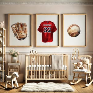 May include: Three framed watercolor prints of baseball-themed items. The prints include a baseball glove, a red jersey with the word "Dukes" and the number 32, and a baseball. The prints are in a nursery setting.