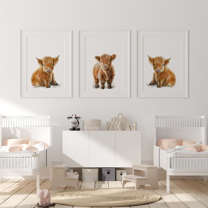 May include: Three framed watercolor prints of Highland calves. Each calf has shaggy, reddish-brown fur and is set against a white background. The prints are displayed above a white cabinet in a child's bedroom.
