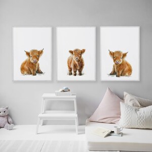 May include: Set of three framed art prints featuring watercolor illustrations of Highland calves. Each calf has reddish-brown fur and is depicted on a white background. The prints are displayed in a child's room, with a white step stool and decorative pillows.