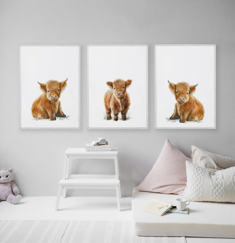 May include: Set of three framed art prints featuring watercolor illustrations of Highland calves. Each calf has reddish-brown fur and is depicted on a white background. The prints are displayed in a child's room, with a white step stool and decorative pillows.