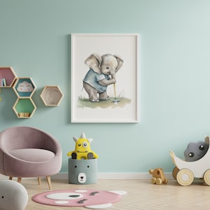 Puede incluir: Una pintura de acuarela de un elefante beb&eacute; jugando al golf, enmarcada en un marco blanco, colgada en una pared azul claro. La pintura est&aacute; rodeada de una variedad de juguetes para ni&ntilde;os, incluyendo una jirafa de peluche, un monstruo de peluche y un cochecito de juguete de madera.