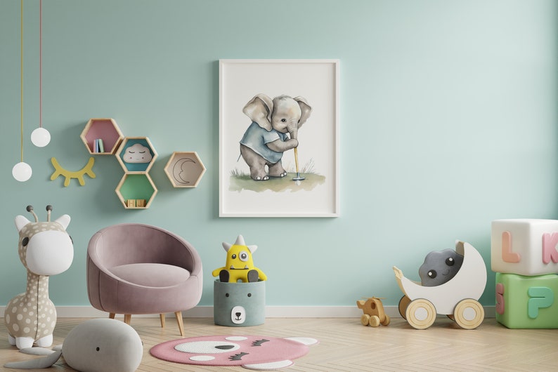 Puede incluir: Una pintura de acuarela de un elefante beb&eacute; jugando al golf, enmarcada en un marco blanco, colgada en una pared azul claro. La pintura est&aacute; rodeada de una variedad de juguetes para ni&ntilde;os, incluyendo una jirafa de peluche, un monstruo de peluche y un cochecito de juguete de madera.