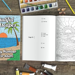 May include: A color-by-number book for adults titled "Beautiful Landscapes" with a cover illustration of a beach scene with palm trees and a sunset. The open book shows a line drawing of a sailboat on the ocean. Art supplies are scattered around.