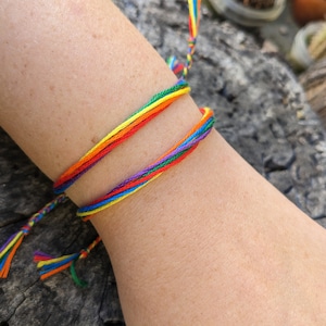 May include: A rainbow friendship bracelet made of colorful string. The bracelet is tied around a person's wrist.