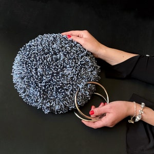 May include: A round, blue and silver, fluffy handbag with two silver ring handles.