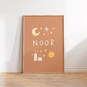 Puede incluir: Una impresión enmarcada con un fondo melocotón que presenta una luna creciente, estrellas, velas, un sol y la palabra "NOOR" en letras blancas.