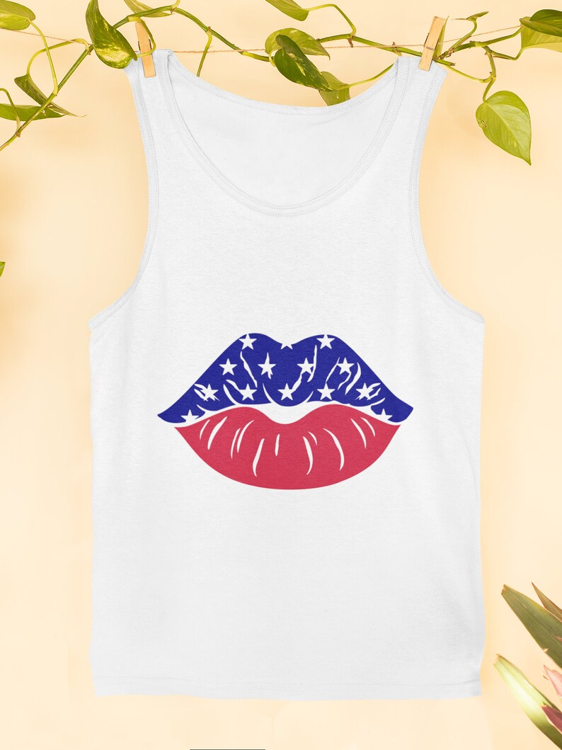 May include: White vest top with a graphic of lips. The upper lip is blue with white stars, and the lower lip is red. The vest top is hanging on a clothesline with green vines.