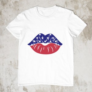 May include: White t-shirt with a graphic of lips. The upper lip is blue with white stars, and the lower lip is red. The design is centered on the shirt, creating a patriotic theme.
