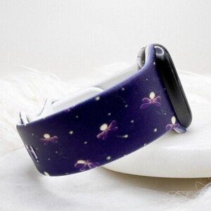 May include: A dark purple silicone watch band featuring a repeating pattern of small, stylized purple dragonflies with white glowing bodies. The band is attached to a black watch connector piece and has a smooth, matte finish throughout the surface.