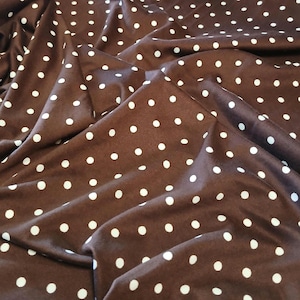 Peut inclure: Tissu marron à pois blancs. Le tissu est drapé, créant des plis et des ombres qui ajoutent de la profondeur. Les pois sont espacés uniformément et de tailles variables.