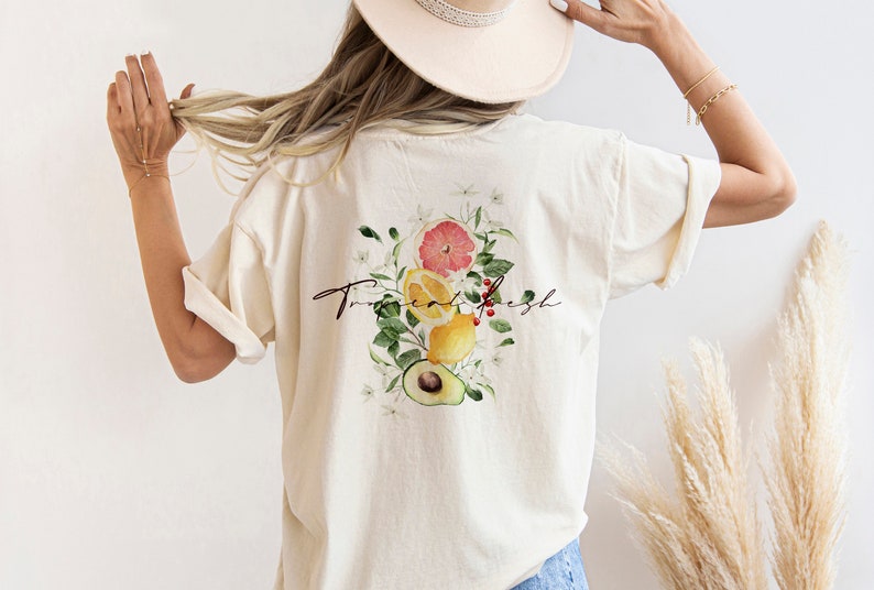 May include: A white t-shirt with a graphic of a grapefruit, lemons, and an avocado with green leaves and white flowers. The text "True & Fresh" is written in cursive on the shirt.