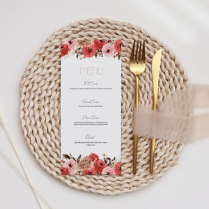 Puede incluir: Una tarjeta de men&uacute; blanca con un dise&ntilde;o floral y la palabra "MENU" en letras doradas. La tarjeta est&aacute; colocada sobre un mantel individual tejido con un tenedor y un cuchillo dorados.