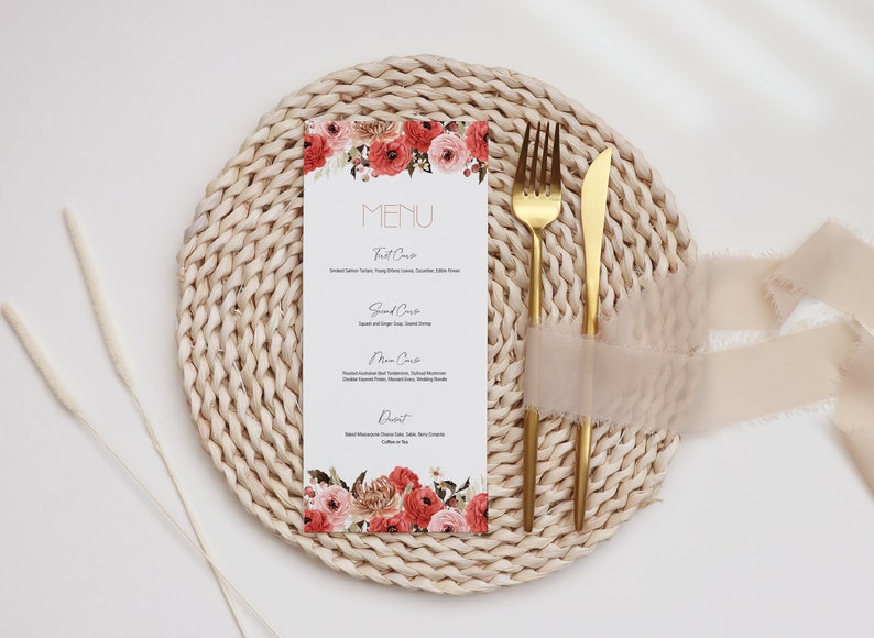 Puede incluir: Una tarjeta de men&uacute; blanca con un dise&ntilde;o floral y la palabra "MENU" en letras doradas. La tarjeta est&aacute; colocada sobre un mantel individual tejido con un tenedor y un cuchillo dorados.