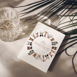 May include: A white card featuring the text "My Friends" encircled by watercolour illustrations of animals such as pandas, giraffes, and zebras. A clear, patterned glass is positioned to the left. Palm leaves are in the background.