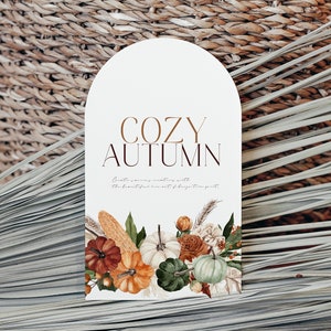 Peut inclure: Une carte blanche avec le texte "COZY AUTUMN" en lettres brunes. La carte pr&eacute;sente une illustration aquarelle de citrouilles, de ma&iuml;s et de fleurs.