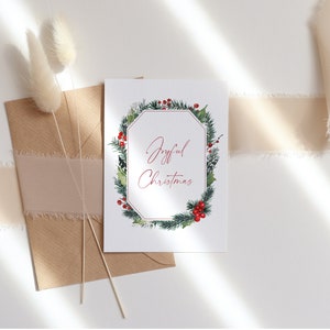 K&ouml;nnte beinhalten: Eine wei&szlig;e Karte mit einem gr&uuml;nen und roten Weihnachtskranz-Design. Der Text "Joyful Christmas" ist in roter Kursivschrift innerhalb des Kranzes geschrieben.