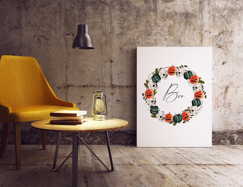 May include: A white printable art print with a Halloween wreath featuring orange and green pumpkins, skulls, and vines. The wreath surrounds the word "Boo" in black script.