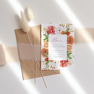 May include: A white invitation card with watercolor illustrations of citrus fruits, flowers, and greenery. The text on the card reads "Marie, Please join us for our wedding, Sunday, 27 December, Saint Presbyterian Church, Celebration to follow, 123 Street, New York, New York, RSVP to 123-456-7890".