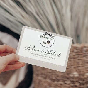 Puede incluir: Una tarjeta de invitaci&oacute;n de boda con una ilustraci&oacute;n de adorno negro y dorado. La tarjeta es beige con un borde blanco y el texto "Andrea & Michael" en letra cursiva negra. La fecha "November 23, 2023" y la ubicaci&oacute;n "Cafe FLOWER" est&aacute;n impresas debajo de los nombres.