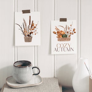 Peut inclure: Deux impressions d'art imprimables sur le th&egrave;me de l'automne. Les impressions pr&eacute;sentent des illustrations &agrave; l'aquarelle de fleurs s&eacute;ch&eacute;es et de courges dans des paniers. Le texte sur l'une des impressions est "Cozy Autumn".