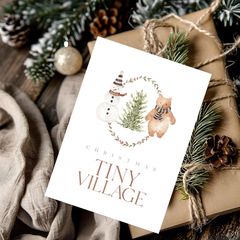 May include: A Christmas card with a watercolor illustration of a snowman, a bear, and a Christmas tree inside a wreath. The card reads "CHRISTMAS TINY VILLAGE" in brown text. The card is on a wrapped gift.