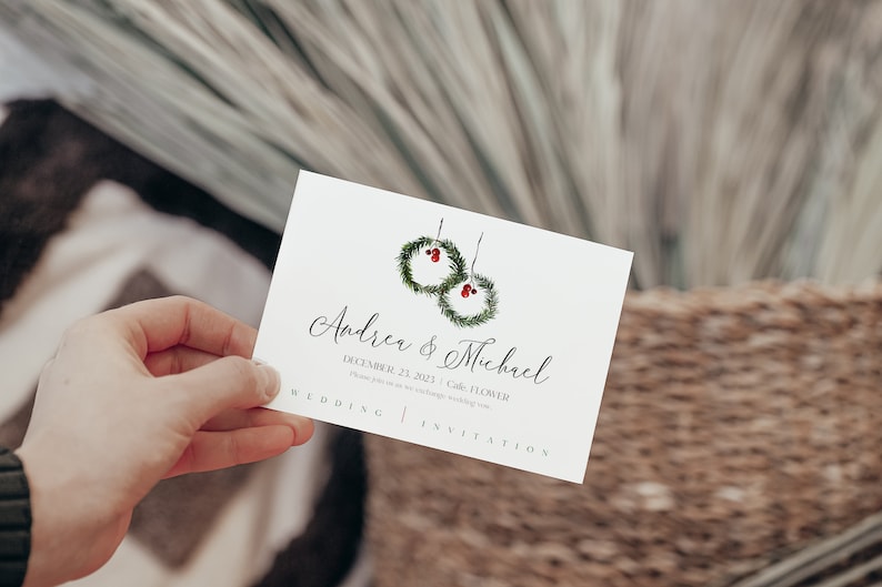 May include: A white wedding invitation with a simple design featuring two green wreaths with red berries. The text reads "Andrea & Michael" and "December 23, 2023 - Cafe, FLOWER. Please join us as we exchange wedding vows."