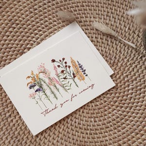 May include: A white card with a floral design and the text "Thank you for coming". The flowers are pressed and dried, and they are in shades of pink, yellow, and purple.