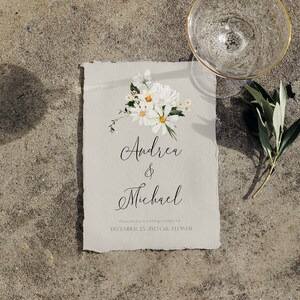 May include: A wedding invitation with a white background and a floral design in the top right corner. The text reads "Andrea & Michael" and "December 27, 2021, Cal. Flower."