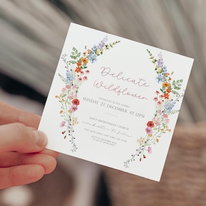 May include: A white invitation card with a floral wreath border. The text reads "Delicate Wildflower" and includes the date and time of the event: "Sunday, 27 December, at 12PM". The invitation is for a wedding celebration.