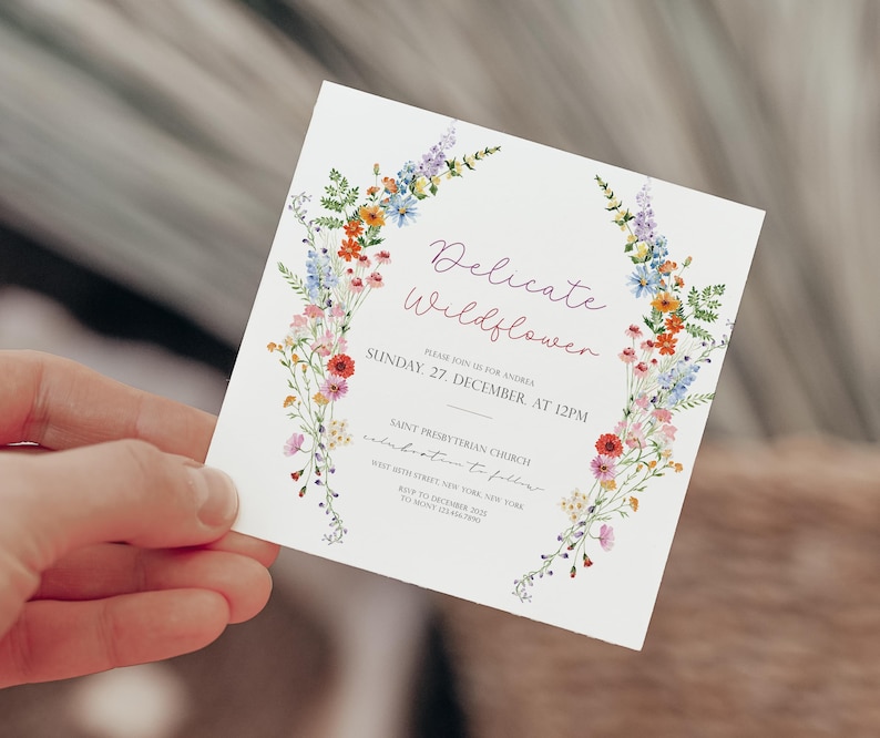 May include: A white invitation card with a floral wreath border. The text reads "Delicate Wildflower" and includes the date and time of the event: "Sunday, 27 December, at 12PM". The invitation is for a wedding celebration.